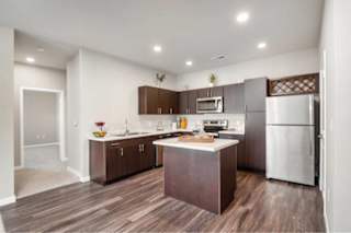 A modern kitchen with dark wood floors and white walls at Aventura at Wentzville I & II Apartments, Wentzville, MO, 63385