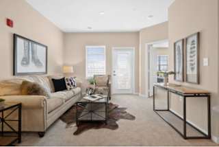 A living room with a white couch, a coffee table, and a painting of a pair of shoes on the wall at Aventura at Wentzville I & II Apartments, Wentzville, 63385