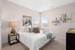 A bedroom with a large bed, a lamp, and two paintings on the wall at Aventura at Wentzville I & II Apartments, Wentzville, MO, 63385
