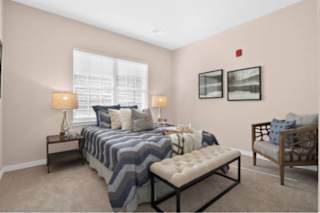 A bedroom with a bed, a bench, and two lamps at Aventura at Wentzville I & II Apartments, Missouri, 63385