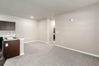 A spacious room with a carpeted floor and a kitchenette in the corner at Aventura at Wentzville I & II Apartments, Missouri, 63385