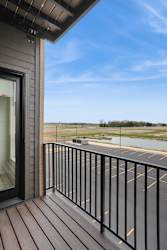 A balcony with a black railing and a view of a parking lot and a field.