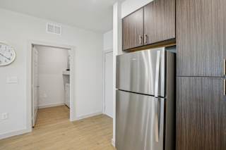 A kitchen with a refrigerator and wooden cabinets. at ThreeTwenty at the Vybe Apartments, Kyle, TX, 78640