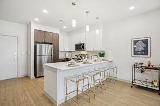 A modern kitchen with a white island and gold bar stools. at ThreeTwenty at the Vybe Apartments, Kyle, 78640