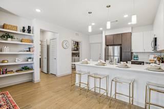 A kitchen with white cabinets and a white island with gold bar stools at ThreeTwenty at the Vybe Apartments, Kyle, Texas