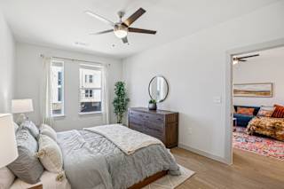 A bedroom with a bed, dresser, mirror, and a ceiling fan. at ThreeTwenty at the Vybe Apartments, Kyle