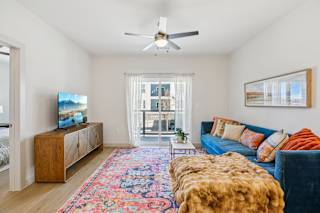 A living room with a blue couch and a wooden cabinet at ThreeTwenty at the Vybe Apartments, Kyle, Texas