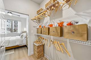 A room with a bed, a window, and a wall-mounted shelf with baskets and bags.