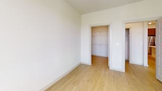 A room with white walls and wooden flooring, with a doorway leading to another room. at ThreeTwenty at the Vybe Apartments, Texas