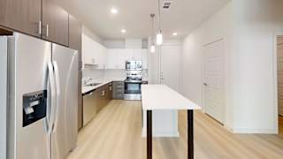 A modern kitchen with a refrigerator on the left and a table in the middle.