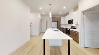 A white table with a black base is in the middle of a room with wooden floors and white walls. at Bridge at Saffron Apartments, Texas