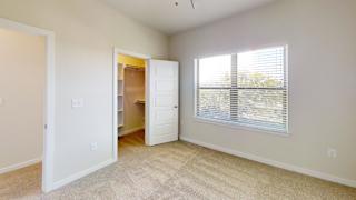 A room with a carpeted floor, a window with blinds, and a closet with an open door. at Bridge at Speyside Apartments, Austin, TX, 78754