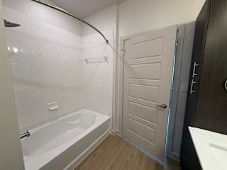 A white tiled bathroom with a white bathtub and a white door.