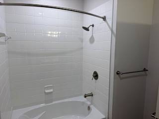 A white tiled bathroom with a white tub and a shower head.