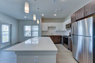 Modern kitchen with large white island and pendant lights at Cantarra Apartments, Manor, 78653