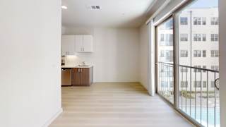 A spacious room with a kitchen area and a balcony with a railing.