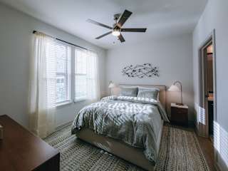 A bedroom with a bed, a ceiling fan, and a window with curtains.