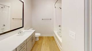 A white bathroom with a wooden floor and a white sink. at Park South Apartments, Texas