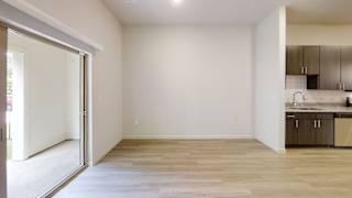 a bedroom with a sliding glass door and a kitchen in the background at Bridge at Three Hills Apartments, Texas