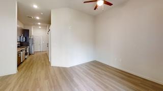 a bedroom with a ceiling fan and a kitchen in the background at Bridge at Three Hills Apartments, Austin, TX, 78747