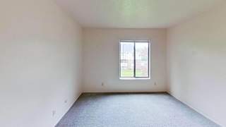 A bedroom with a large window and carpeted floor at Briarwood Apartments in Benton Harbor, MI