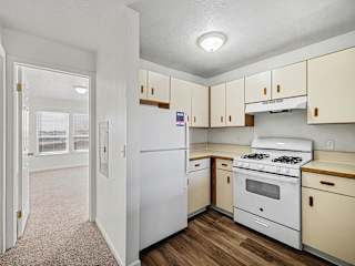 Compact kitchen with white appliances and woodtone flooring at Brentwood Park Apartments, La Vista, Nebraska