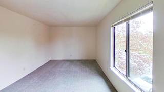 A bedroom with a large window and a carpet at Briarwood Apartments in Benton Harbor, MI