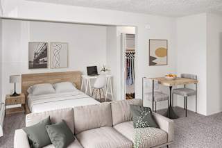 A sleeping area with a bed and a living room with a couch, a chair, and a table at Brookside Apartments, Springfield and a clothing rack.