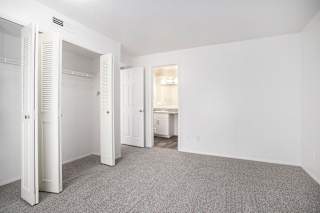 A white bedroom with a carpeted floor and an ensuite bathroom at Canal Club Apartments in Lansing, MI