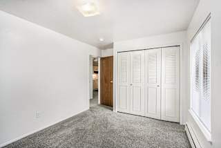 A bedroom with a large window, closet and grey carpet at Concord Place Apartments, Kalamazoo, MI