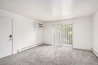A living room with a slider to a balcony, blinds, and a carpeted floor at Concord Place Apartments, Kalamazoo, MI