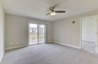 A living room with a ceiling fan and carpeted floor leading to a private balcony at Copper Creek Apartment Homes, Maize, Kansas