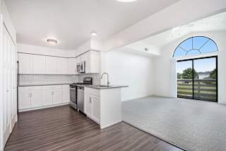 A kitchen with white cabinets and a living room with cathedral ceiling at The Crossings Apartments, Grand Rapids