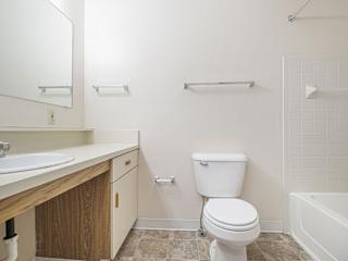A white toilet sits in a bathroom next to a sink and a bathtub at Dupont Lakes Apartments in Fort Wayne, IN