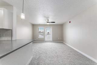 A spacious living room with a ceiling fan and a door leading to a private patio at Eagle Ridge Apartment Homes, Traverse City, Michigan