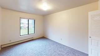 A spacious bedroom with a window and a carpeted floor at Glen Oaks Apartments, Michigan, 49442