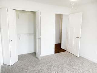 an empty bedroom with white closet doors and a carpet at Meadowbrooke Apartment Homes, Grand Rapids