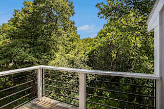 A balcony with a metal railing overlooks a wooded area at Pine Knoll Apartments, Battle Creek, 49014