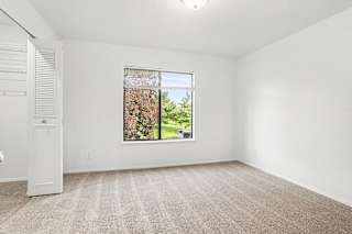 A bedroom with a carpeted floor and a large window showing a tree outside at Pine Knoll Apartments, Battle Creek
