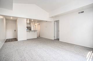 A large, empty living room with a cathedral ceiling and carpeted floor at Pine Knoll Apartments, Battle Creek, 49014