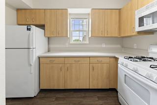 A kitchen with a window, wooden cabinets and white appliances at Stoney Pointe Apartment Homes, Kansas