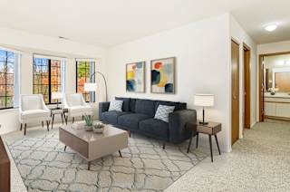 A living room with a bay window,  grey couch, and a coffee table  at Tanglewood Apartments, Oak Creek, WI