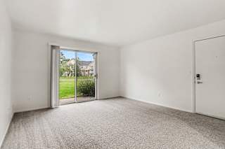 A living room with a carpeted floor and a sliding glass door leading to a patio and green lawn at Walnut Trail Apartments, Michigan