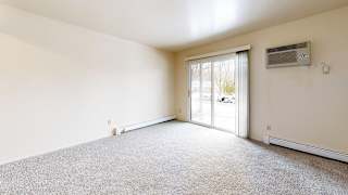 A living room with a carpeted floor, sliding glass doors, and a window with blinds at Wood Creek Apartments, Kenosha, WI, 53144