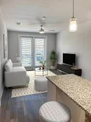 A living room with a grey couch, a white ottoman, a television, and a ceiling fan.