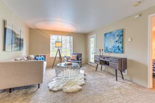 A living room with a beige couch, a glass table, and a painting on the wall.