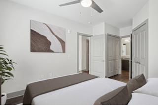 A bedroom with a bed, a ceiling fan, and a painting on the wall.