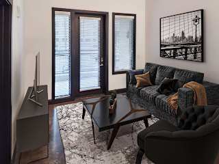 A living room with a grey couch, a black chair, a wooden table, and a television.