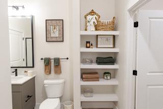 A bathroom with a toilet, sink, and shelves with towels and other items.at District at Riverside Apartments, Chattanooga Tennessee