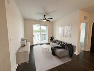 Living room with gray sectional and balcony access at The Wren Apartments, Lawrenceville, Georgia